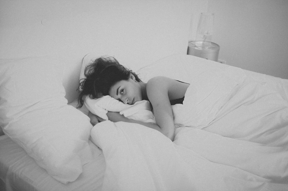 白い毛布で覆われたベッドに横たわる女