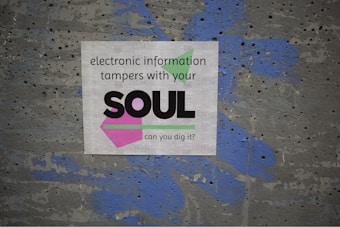 A poster on a concrete wall with a motivational message. The text reads: 'electronic information tampers with your SOUL can you dig it?' The poster features bold and colorful elements, including green and pink geometric shapes, and the word 'SOUL' is prominently highlighted in black.