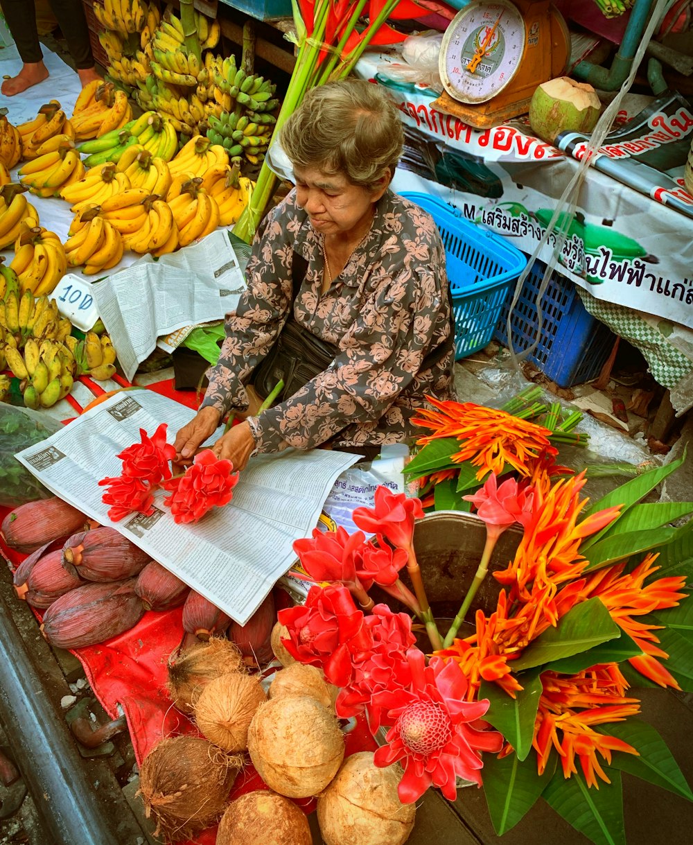 woman fruits and flowers vendor holding red flowers on newspaper