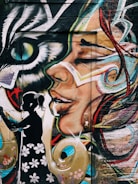 A vibrant and detailed mural painted on a wall. The artwork features a large, colorful face with abstract designs and flowing lines. In the foreground, there's a black silhouette of a girl wearing a dress with flower patterns. An eye that resembles that of a bird or a cat is also part of the mural, giving it a mystical vibe.