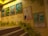 A staircase scene with framed anime movie posters mounted on a wall. The posters include colorful illustrations and Japanese text. The wall is decorated with green leaves and cartoon-like creatures, enhancing a playful and artistic ambiance.