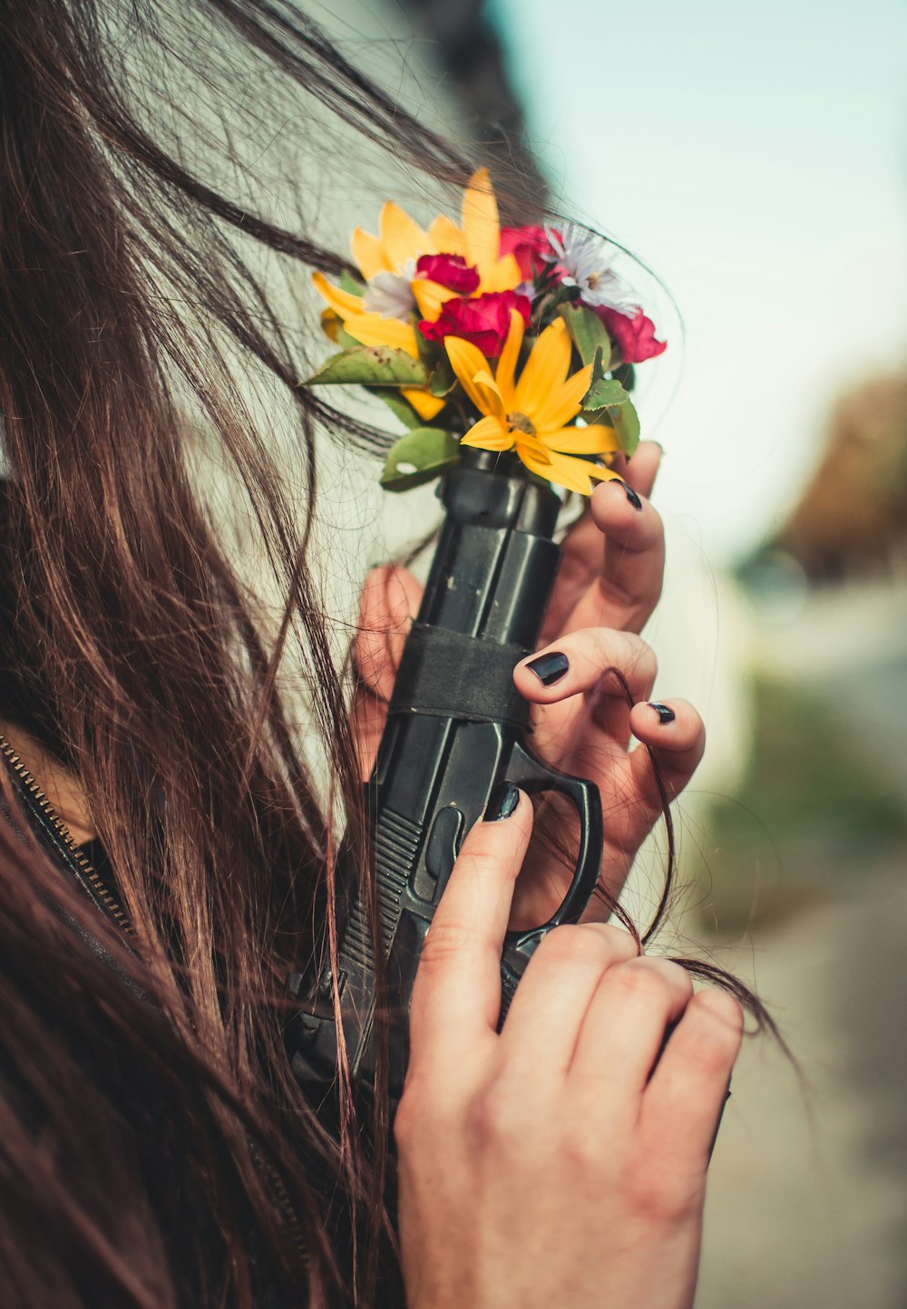 person holding automatic pistol with multicolored flowers on tip