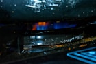 A close-up of a gas stove burner with a blue flame underneath a dark, slightly corroded metal grate. The surrounding area is dark with hints of rust and grime.