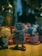 A collection of toys is displayed on a wooden surface, including a vintage-style robot with a square body and red feet, alongside an assortment of colorful figures and decorative items. The background is slightly out of focus, creating a cozy, cluttered atmosphere.
