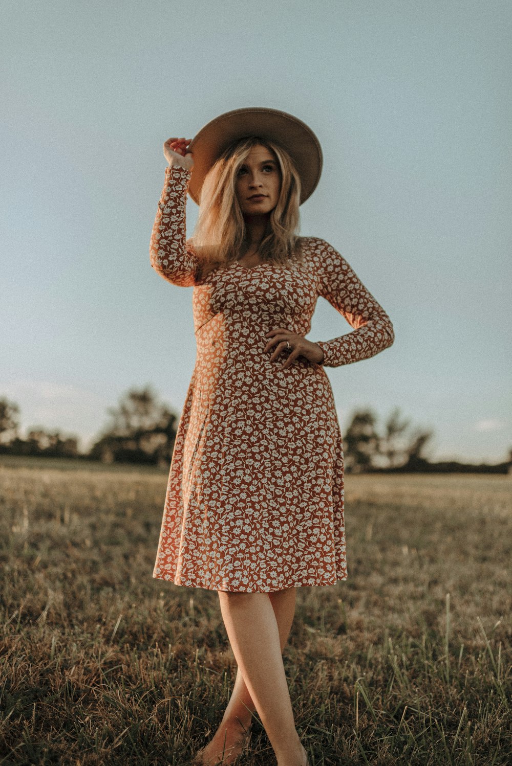 a woman in a dress and hat standing in a field