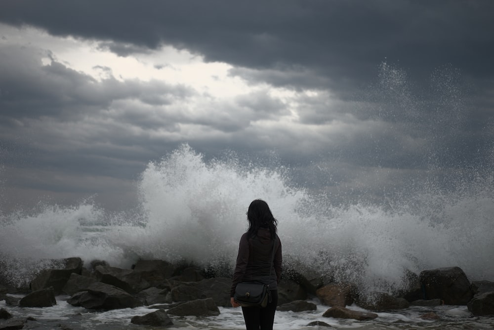 Photographie de silhouette de femme debout au bord de la mer regardant les éclaboussures des vagues