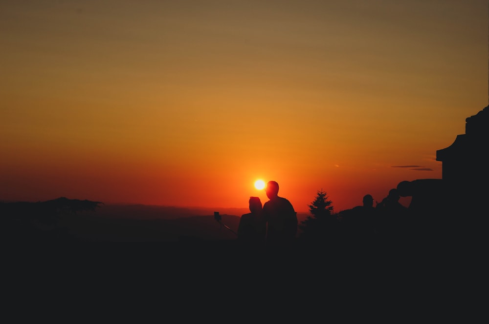 um casal de pessoas em pé no topo de uma colina ao pôr do sol