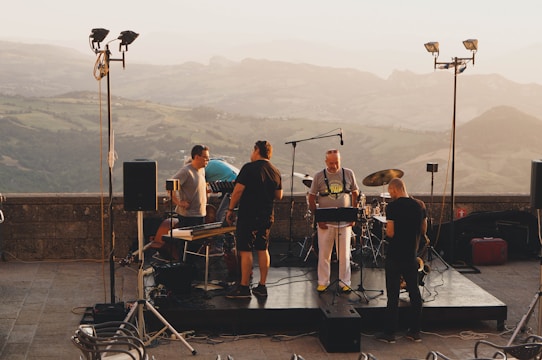 A group of young singers performing passionately on a rustic stage with mountain backdrop.