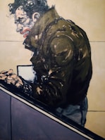 A stylized painting of a person in a dark jacket, leaning forward with clenched hands. The facial expression is intense, featuring exaggerated features like a pronounced mouth and furrowed brow. The background is mostly plain with subtle color contrasts.