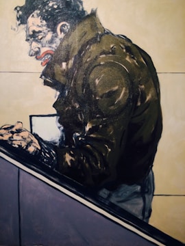 A stylized painting of a person in a dark jacket, leaning forward with clenched hands. The facial expression is intense, featuring exaggerated features like a pronounced mouth and furrowed brow. The background is mostly plain with subtle color contrasts.