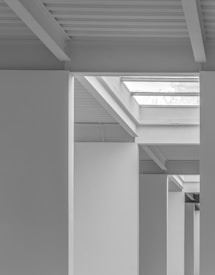 A series of architectural elements featuring clean, linear forms and a monochromatic color scheme. The image focuses on structural beams, columns, and skylights, creating a minimalist and modern design aesthetic.