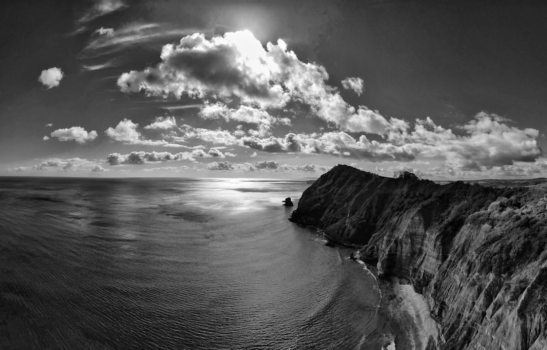 grayscale photograhy of mountain cliff and seashore during daytime