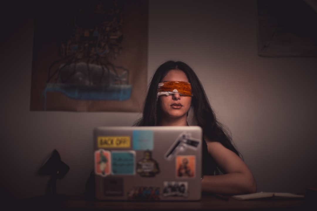 woman with blindfold sitting in front of a laptop