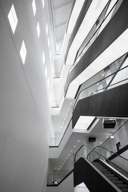 An abstract architectural interior featuring modern design elements with angular lines and bright lighting. The multi-story structure showcases several levels with glass railings and recessed lighting, conveying a sense of space and openness.