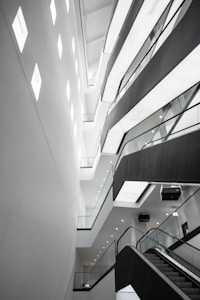 An abstract architectural interior featuring modern design elements with angular lines and bright lighting. The multi-story structure showcases several levels with glass railings and recessed lighting, conveying a sense of space and openness.
