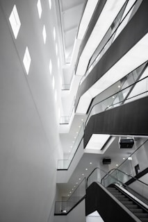 An abstract architectural interior featuring modern design elements with angular lines and bright lighting. The multi-story structure showcases several levels with glass railings and recessed lighting, conveying a sense of space and openness.