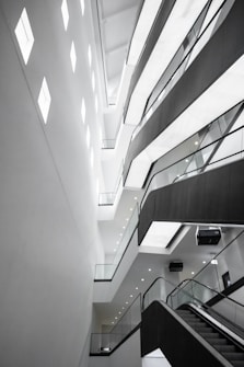 An abstract architectural interior featuring modern design elements with angular lines and bright lighting. The multi-story structure showcases several levels with glass railings and recessed lighting, conveying a sense of space and openness.