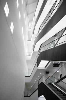 An abstract architectural interior featuring modern design elements with angular lines and bright lighting. The multi-story structure showcases several levels with glass railings and recessed lighting, conveying a sense of space and openness.