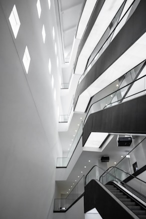 An abstract architectural interior featuring modern design elements with angular lines and bright lighting. The multi-story structure showcases several levels with glass railings and recessed lighting, conveying a sense of space and openness.