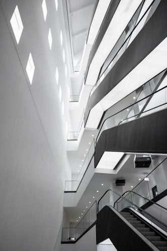 An abstract architectural interior featuring modern design elements with angular lines and bright lighting. The multi-story structure showcases several levels with glass railings and recessed lighting, conveying a sense of space and openness.