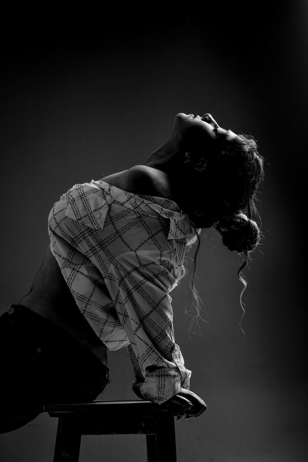 grayscale photography of woman sitting on a stool leaning backwards