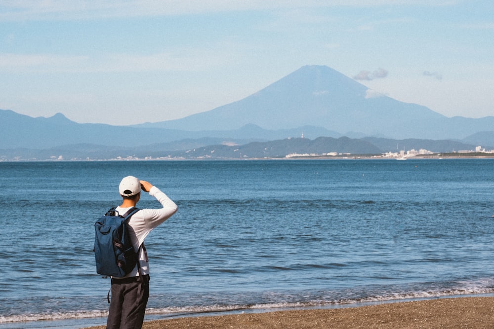 man in white cap and blue backpack standing in seashore