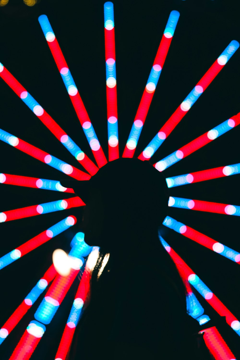 Una persona parada frente a una noria con luces rojas, blancas y azules
