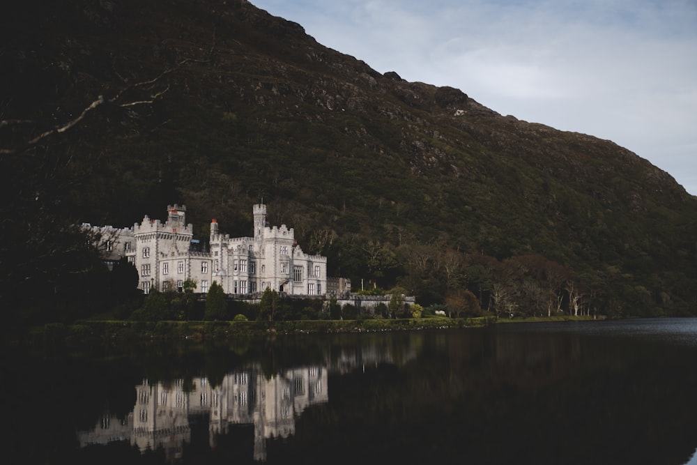 Castelo branco ao lado da montanha e corpo de água durante o dia