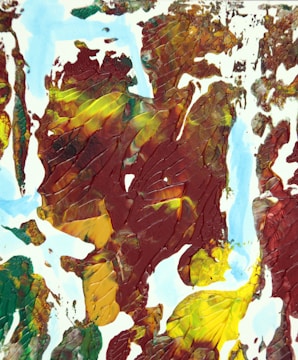 An abstract painting featuring thick, textured layers of paint. The colors blend into one another with visible brush strokes and a dominant presence of earthy tones. The composition includes a mixture of dark red, green, yellow, and blue, creating an impression of movement and depth.