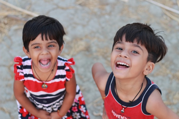 Two kids laughing together, dressed in cozy sweaters and stylish pants from strakorfashion.