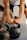 A person is gripping two kettlebells placed on a gym floor. The focus is on the person's forearms and hands, with the kettlebells showing signs of wear. The background is blurred, indicating a gym setting.