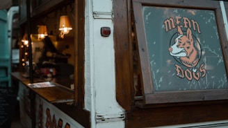 A food truck with wooden accents and a window displaying a sign that reads 'Mean Dogs' accompanied by a cartoon image of a fox. The interior of the truck is warmly lit by small hanging lamps, and there are various items such as containers and possibly food preparation tools visible inside.
