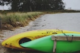 Children playing on the grassy shore with colorful kayaks lined up by the water.