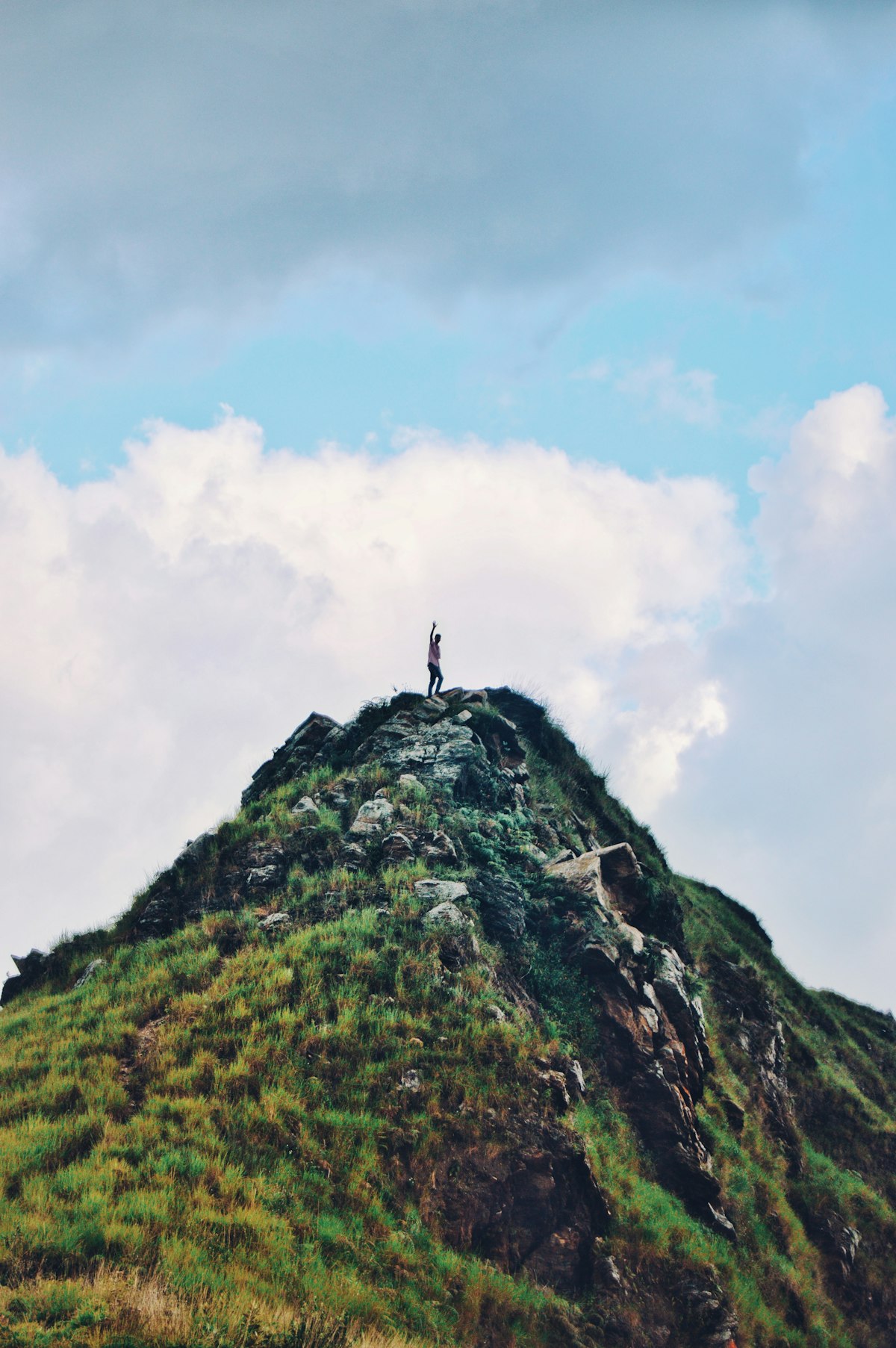 Person standing on a grass-covered mountain, contemplative scale shot