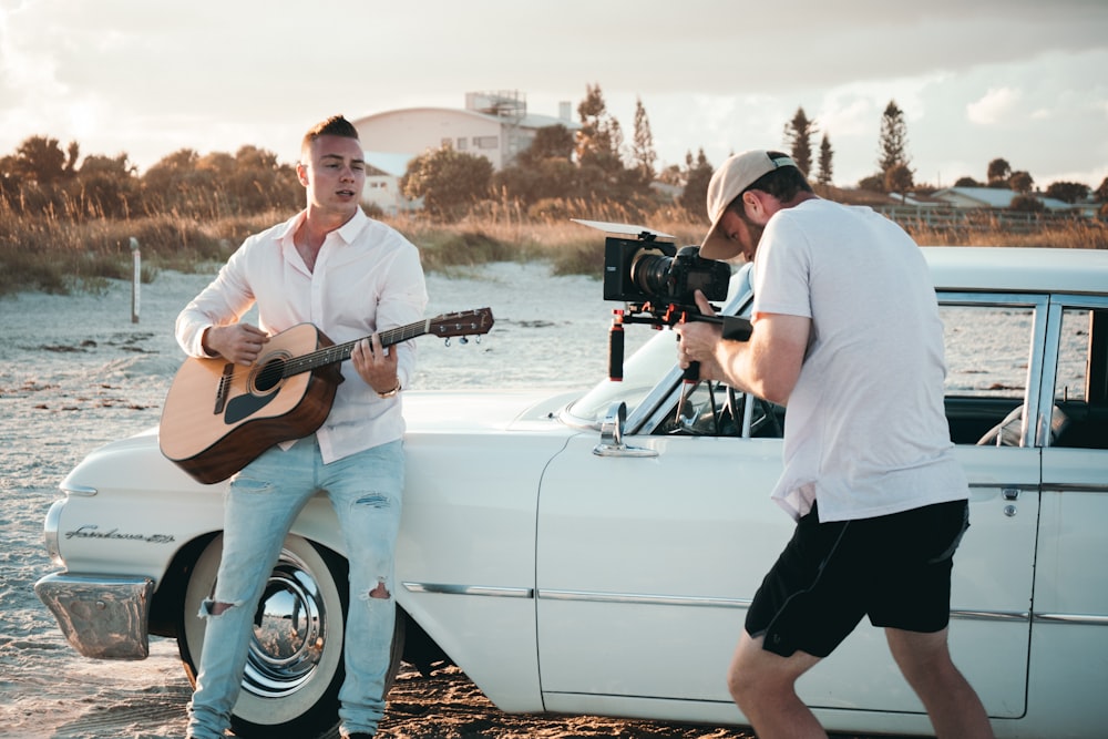 man carrying guitar near car