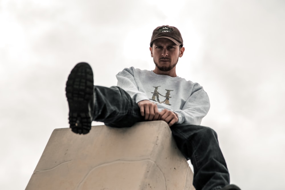 man in gray sweatshirt and black pants sitting on platform under white sky