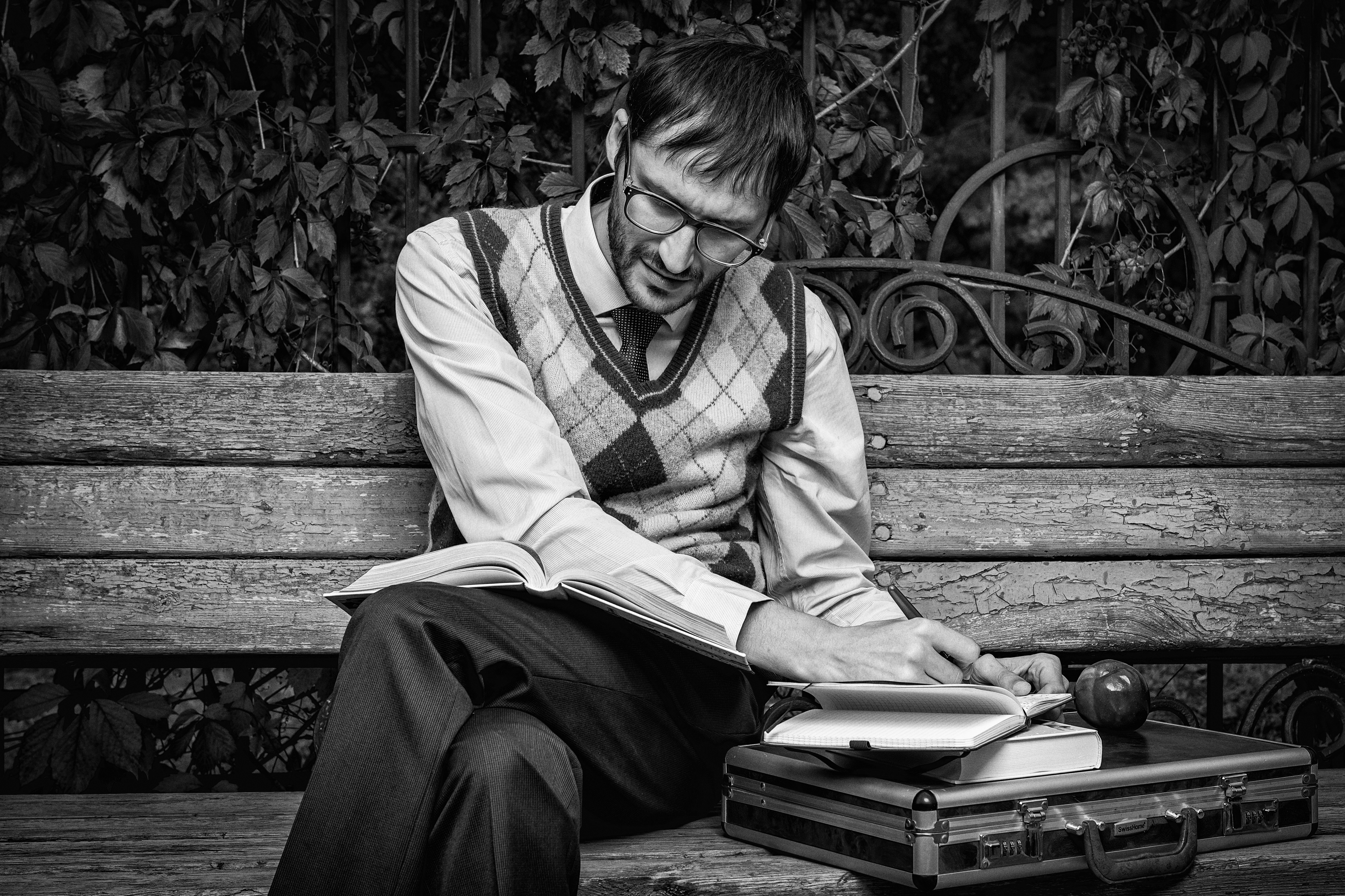 grayscale photo of man in sweater vest sitting on bench