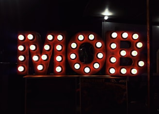 Large letters spelling out 'MOB' are illuminated with round light bulbs, creating a vintage marquee style. The background is dark, highlighting the bright, circular lights on the letters.
