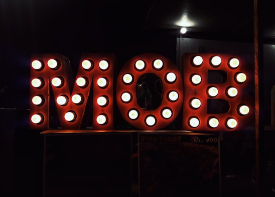 Large letters spelling out 'MOB' are illuminated with round light bulbs, creating a vintage marquee style. The background is dark, highlighting the bright, circular lights on the letters.