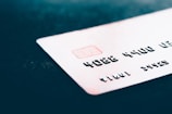 A close-up of a credit card with embossed numbers and a chip, placed on a dark surface. The focus is on the card's details like the numbers and the chip, with the background being blurred.