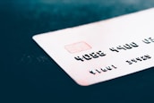 A close-up of a credit card with embossed numbers and a chip, placed on a dark surface. The focus is on the card's details like the numbers and the chip, with the background being blurred.