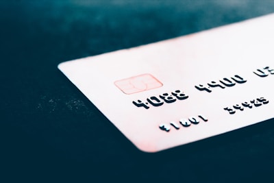 A close-up of a credit card with embossed numbers and a chip, placed on a dark surface. The focus is on the card's details like the numbers and the chip, with the background being blurred.