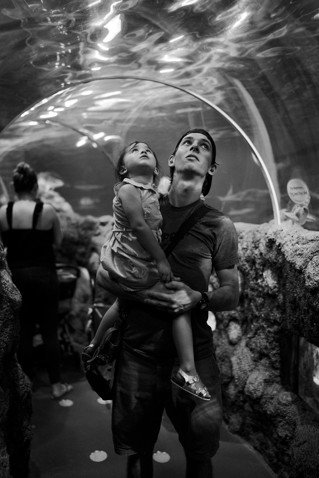 grayscale photography of man carrying a girl inside an aquarium museum