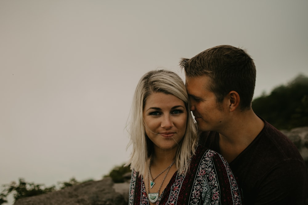 man standing behind smiling woman under gray skies