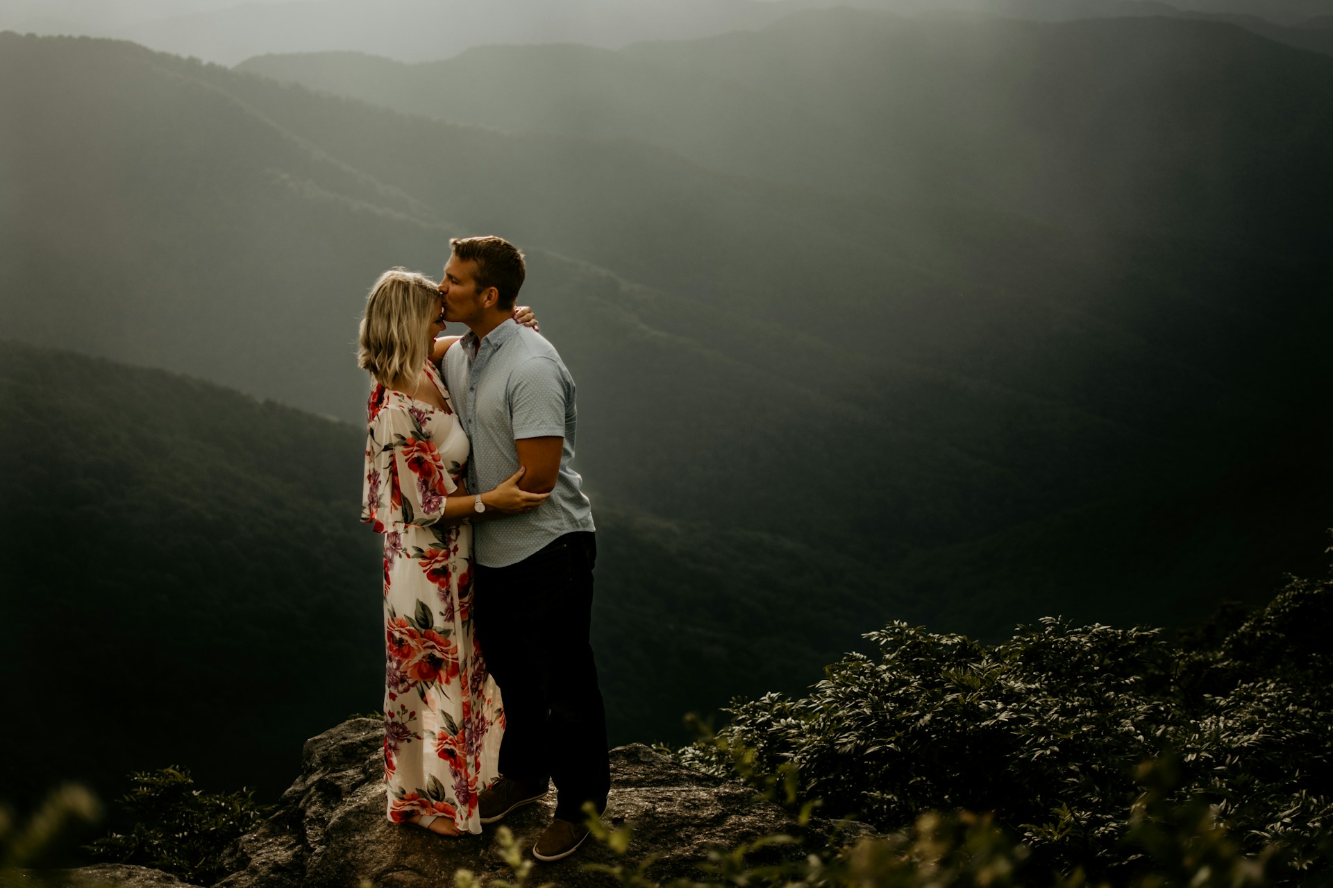 man wearing gray polo shirt kissing a woman in forehead and woman wearing white and red floral dress