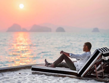 Sunset view of a traveler relaxing on a beach with a travel insurance card in hand.