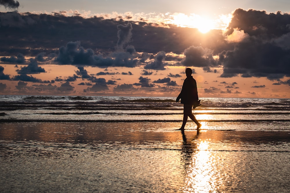 silhouette photography of person walking by the seashore during golden hour