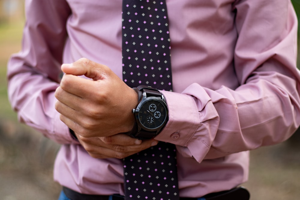 man wears black chronograph watch and pink dress shirt