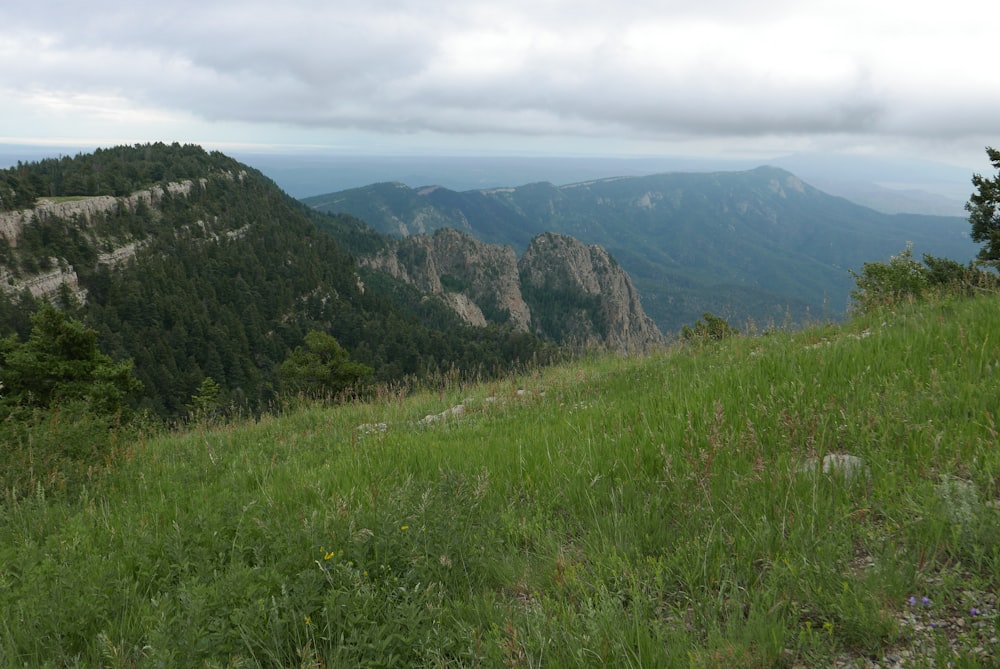 green grass field near mountain under white clouds during daytime