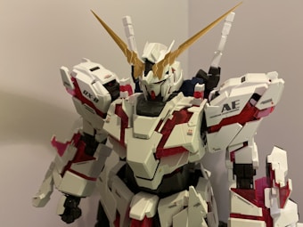 A detailed model of a robot with a sleek, futuristic design featuring angular white armor plates, red accents, and gold horn-like protrusions on the head.